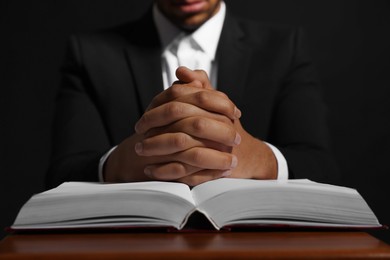 Photo of African American man with Bible praying to God at table on black background, closeup