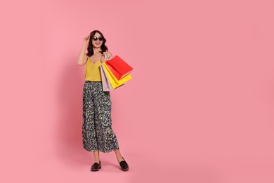 Photo of Beautiful young woman with paper shopping bags on pink background. Space for text