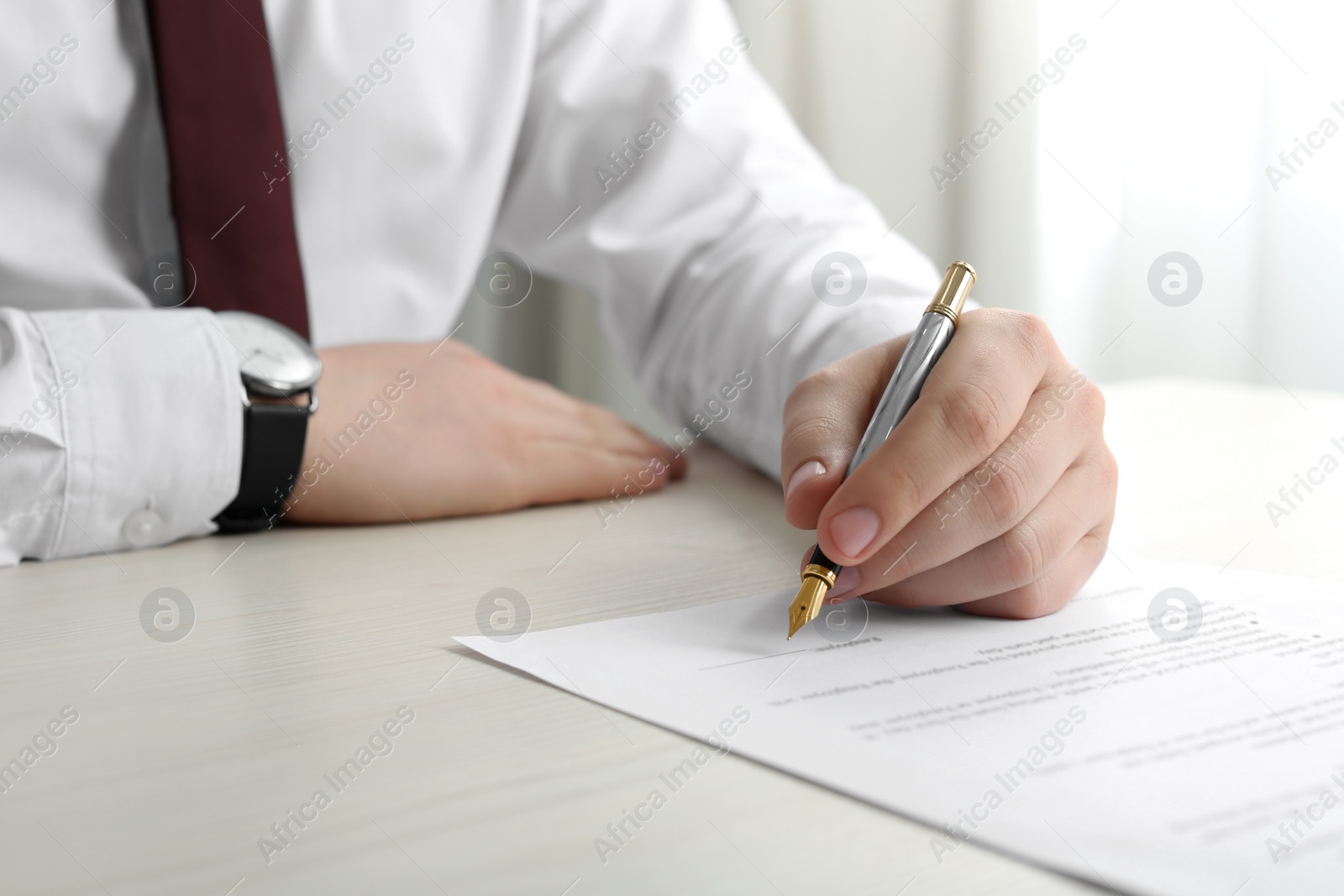 Photo of Notary signing document at wooden table indoors, closeup
