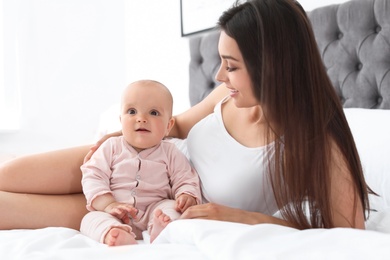 Photo of Young mother with her cute baby girl on bed at home
