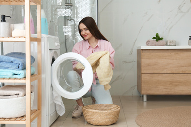 Young woman with clothes near washing machine in bathroom. Laundry day
