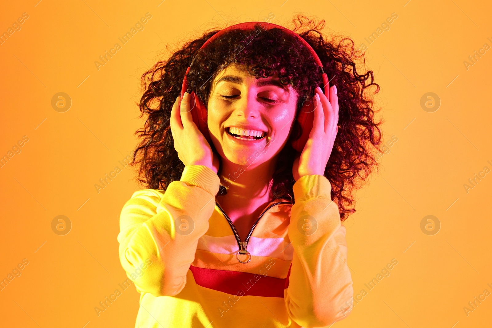 Photo of Beautiful young woman listening to music with headphones on color background in neon lights