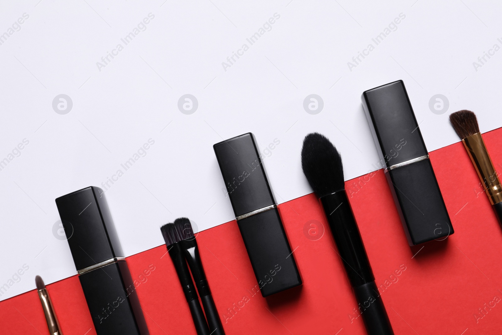 Photo of Lipsticks and different makeup brushes on color background, flat lay