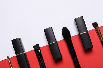 Photo of Lipsticks and different makeup brushes on color background, flat lay
