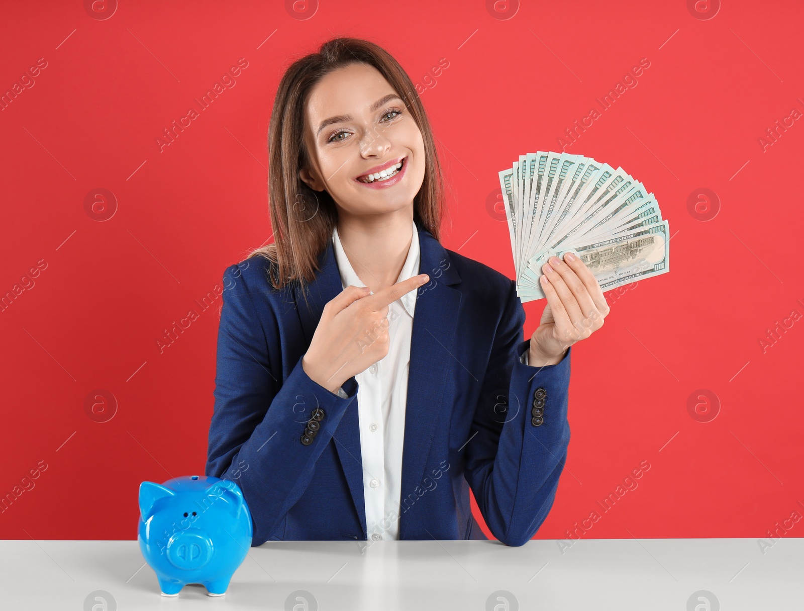 Photo of Young woman with money and piggy bank at table on crimson background