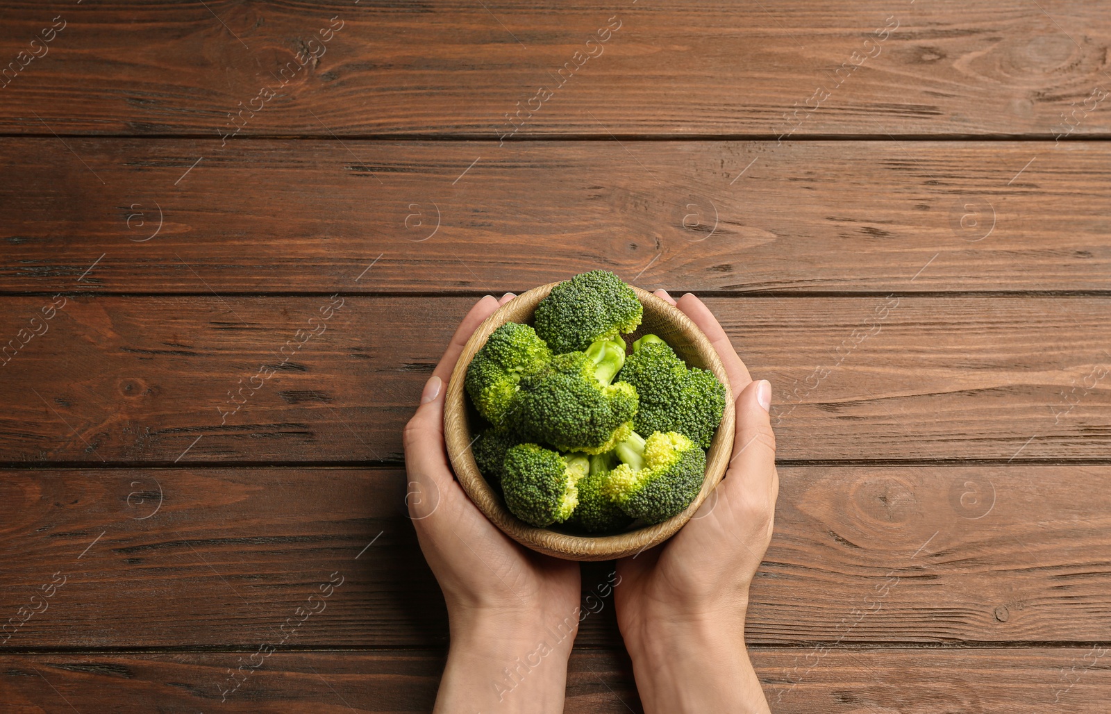 Photo of Female holding bowl of fresh green broccoli on wooden table, top view. Space for text