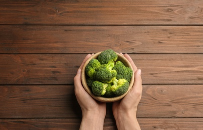 Photo of Female holding bowl of fresh green broccoli on wooden table, top view. Space for text