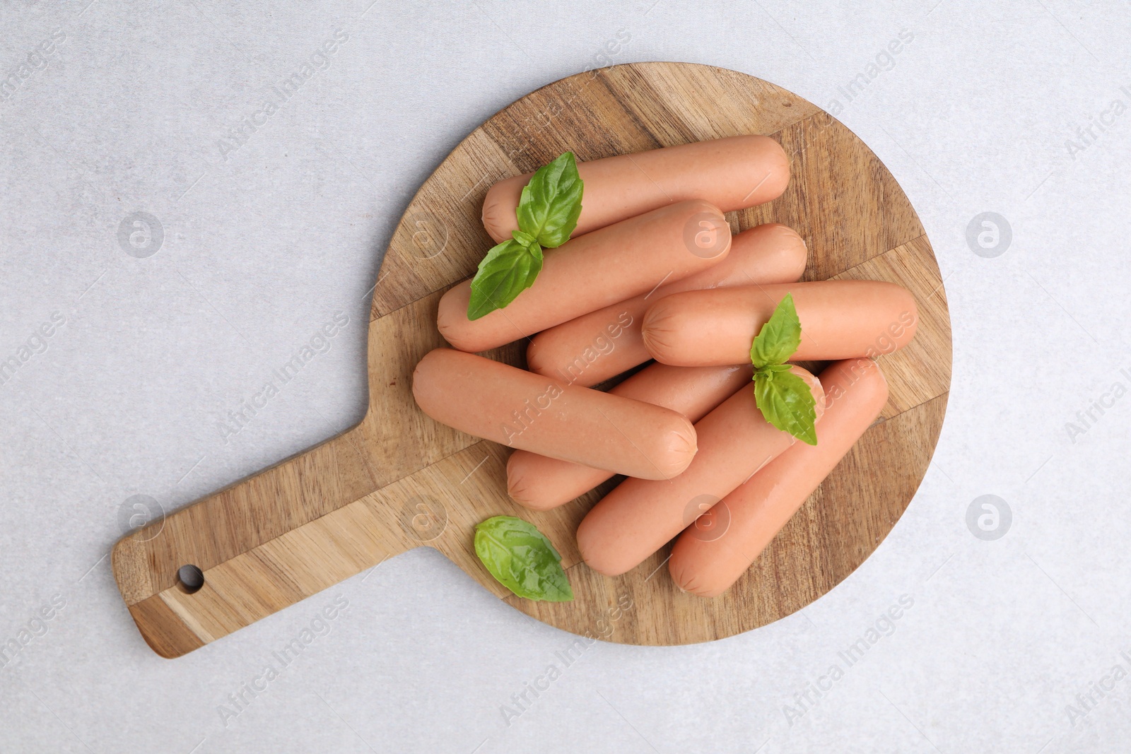 Photo of Delicious boiled sausages and basil on light gray table, top view