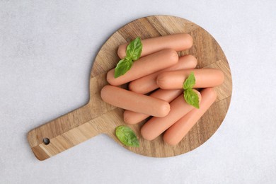 Delicious boiled sausages and basil on light gray table, top view