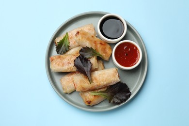 Photo of Tasty fried spring rolls, lettuce and sauces on light blue table, top view