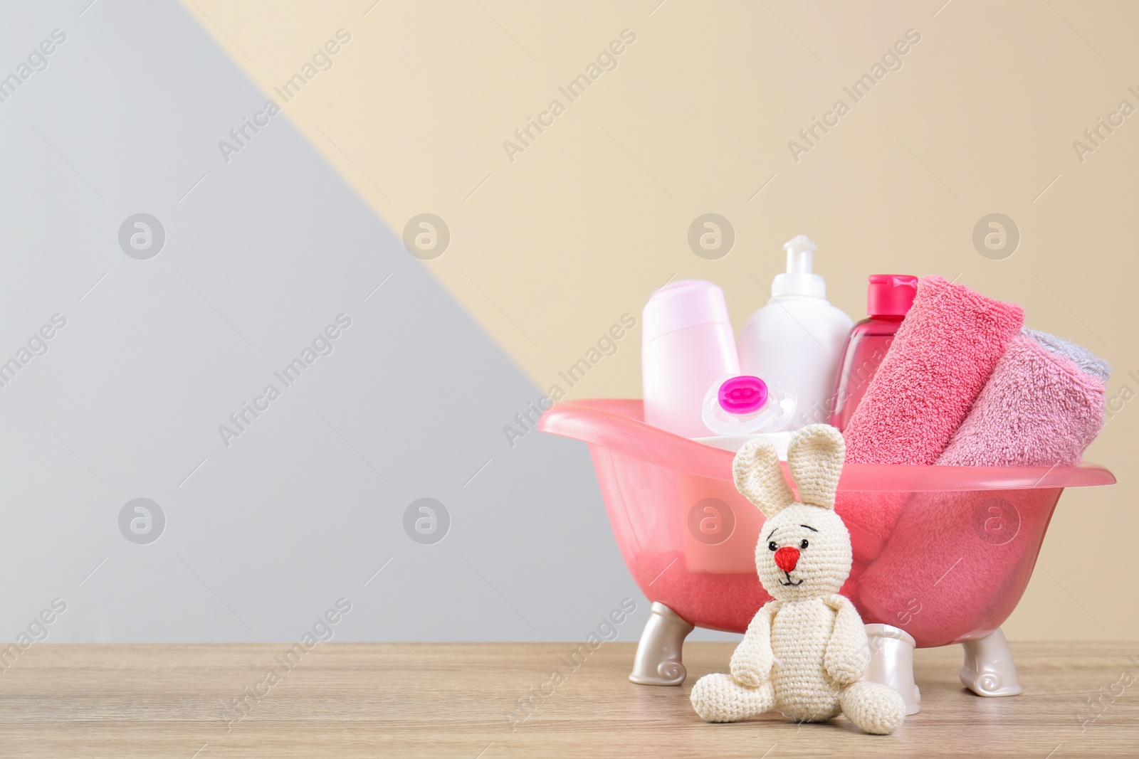 Photo of Baby cosmetic products, knitted rabbit and towels on table against color background. Space for text