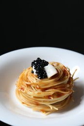 Photo of Tasty spaghetti with tomato sauce and black caviar on dark background, closeup. Exquisite presentation of pasta dish