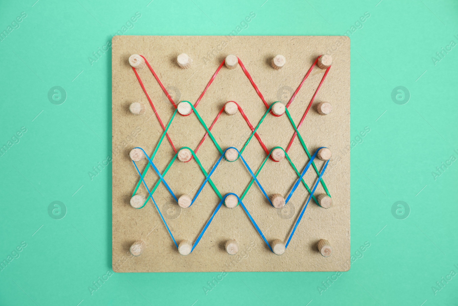 Photo of Wooden geoboard with rubber bands on green background, top view. Educational toy for motor skills development