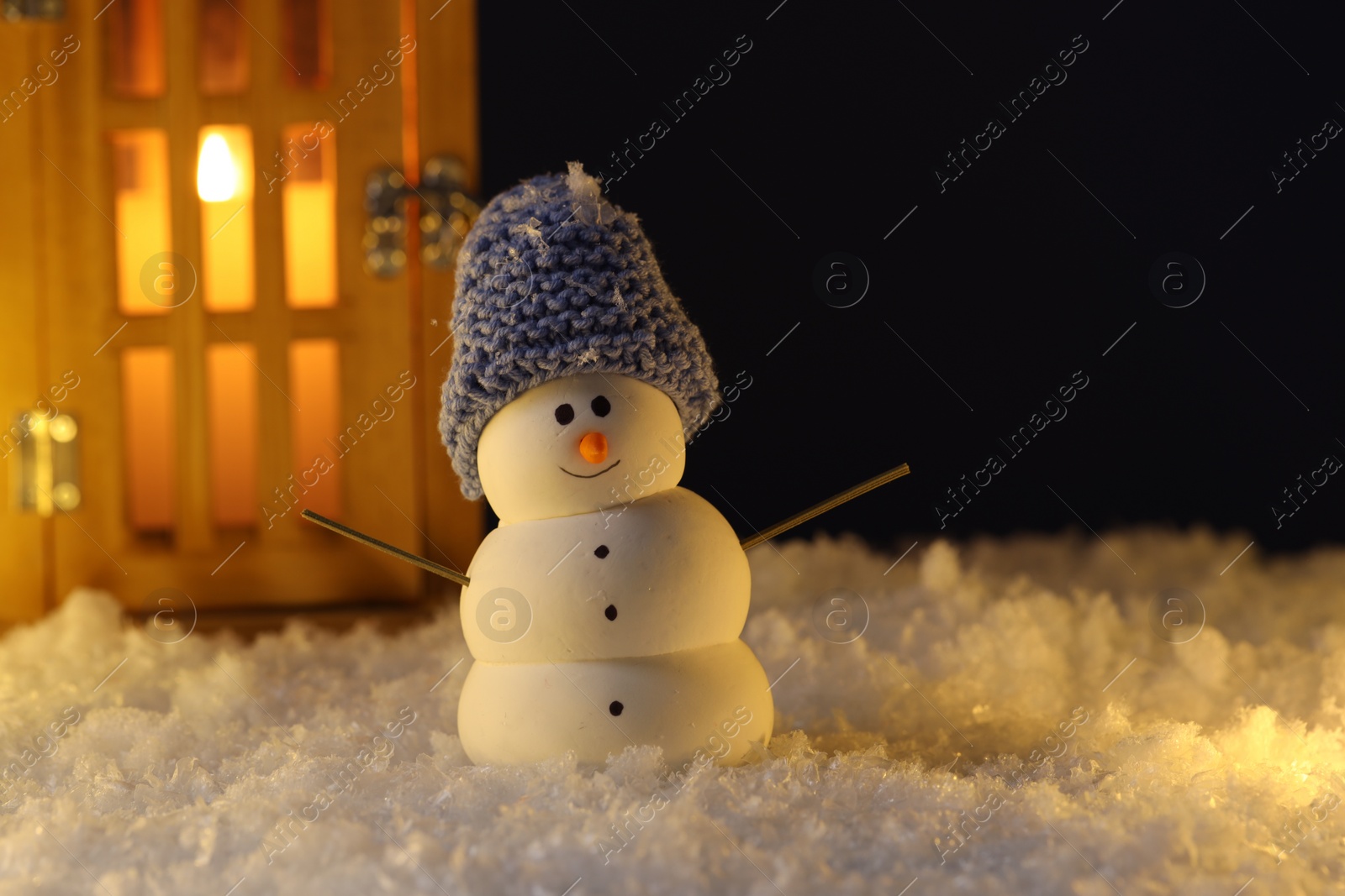 Photo of Cute decorative snowman and lantern on artificial snow against dark background. Space for text