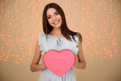 Photo of Portrait of beautiful smiling girl with heart shaped gift box on blurred background. International Women's Day