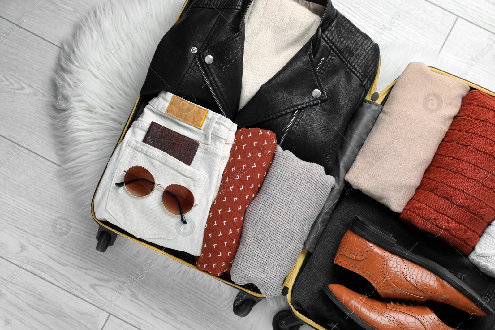 Photo of Open suitcase with folded clothes, shoes and accessories on floor, top view