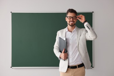 Photo of Happy teacher with glasses and stationery at blackboard in classroom. Space for text