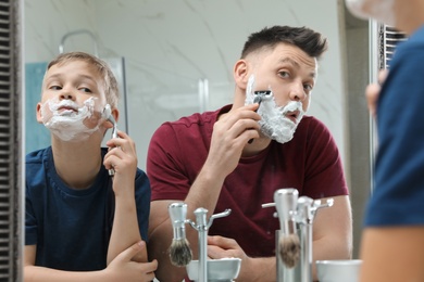 Photo of Dad shaving and son imitating him at mirror in bathroom