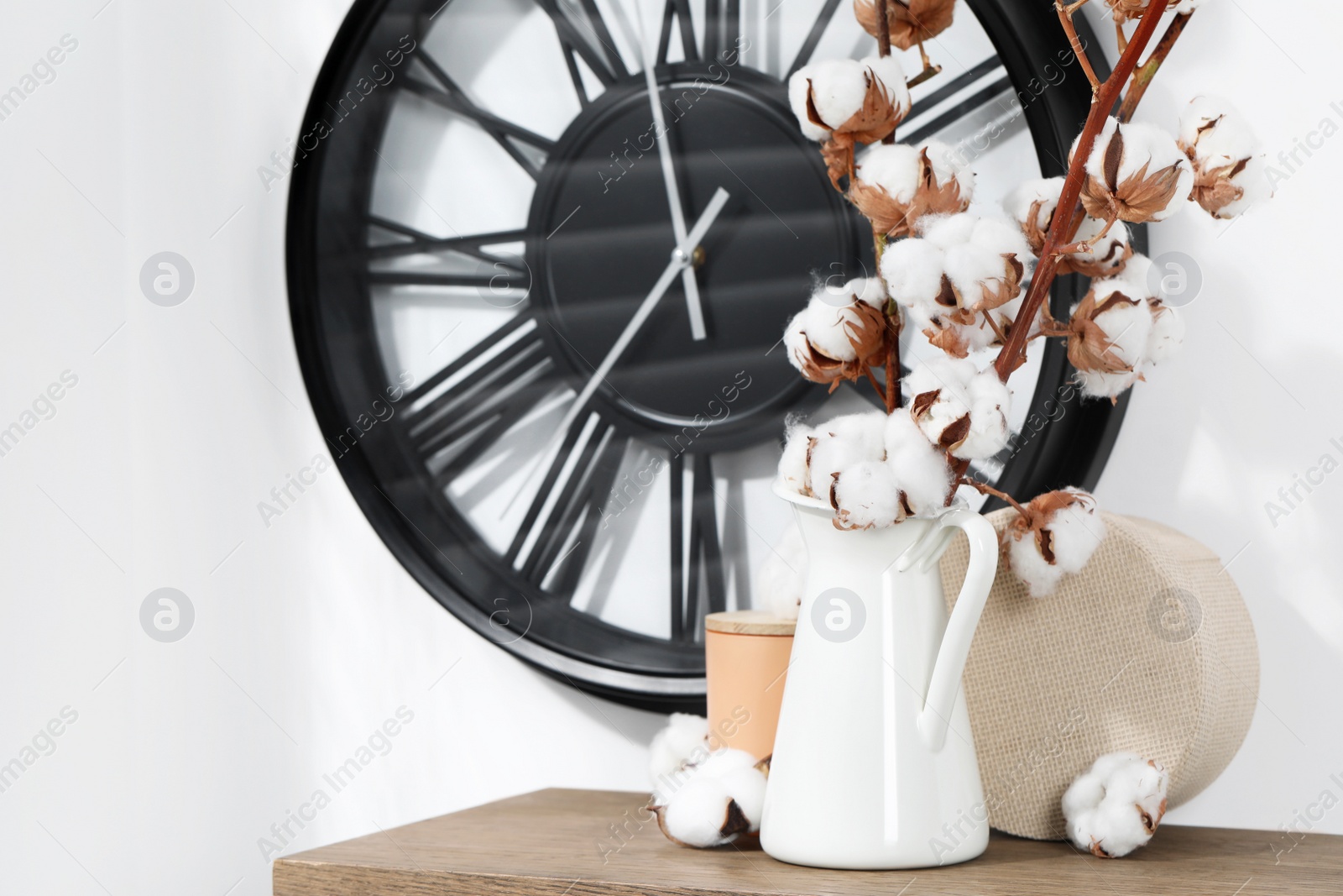 Photo of Cotton branches with fluffy flowers and home decor on wooden table near white wall. Space for text