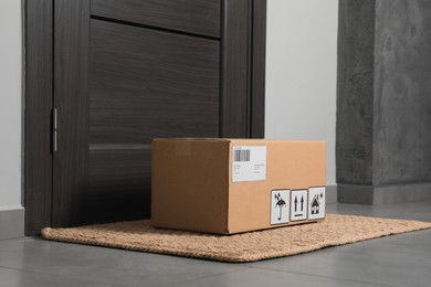 Photo of Cardboard box on floor mat near entrance. Parcel delivery service