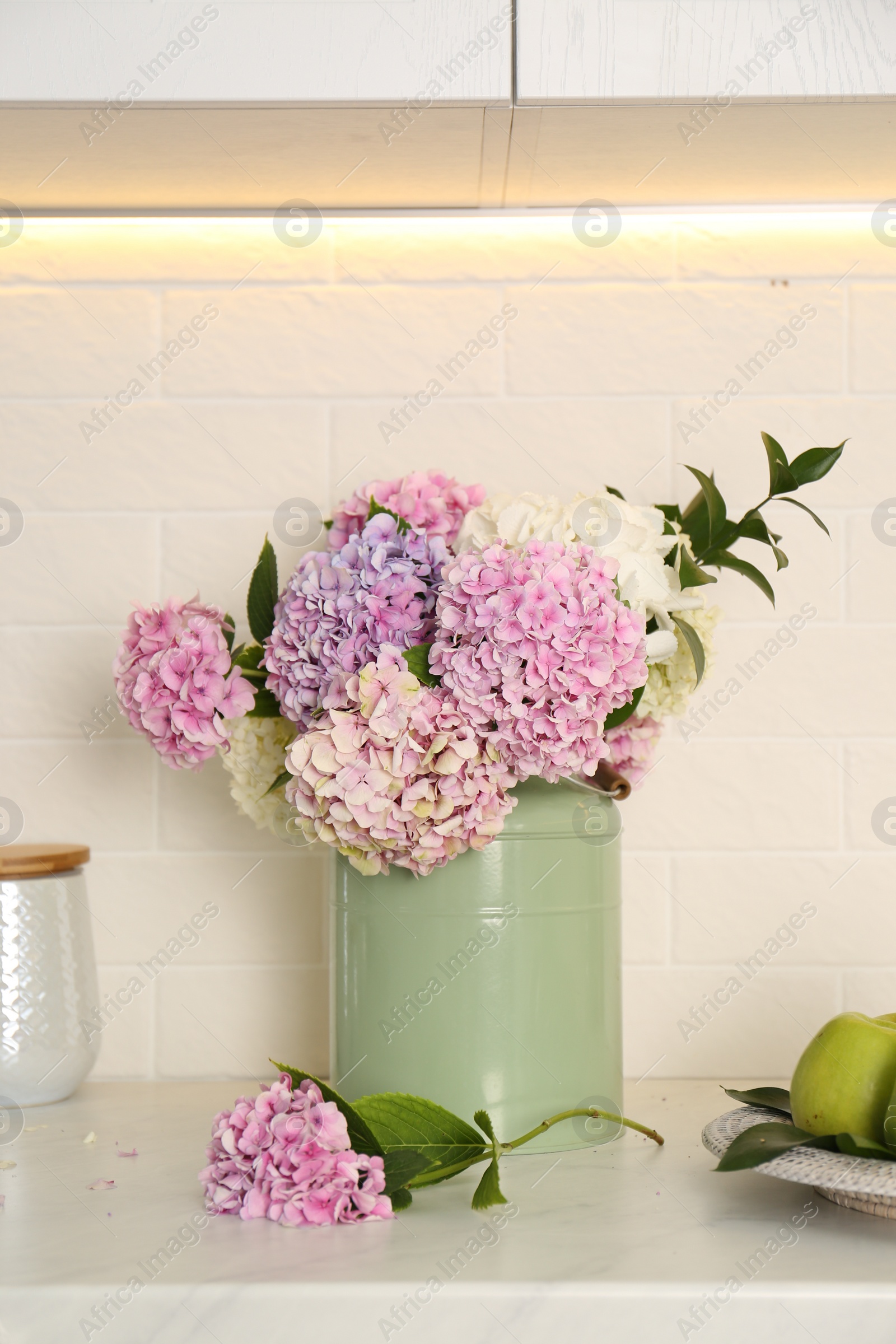 Photo of Beautiful hydrangea flowers in green can on light countertop