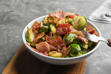Photo of Delicious roasted Brussels sprouts with bacon served on grey table, closeup