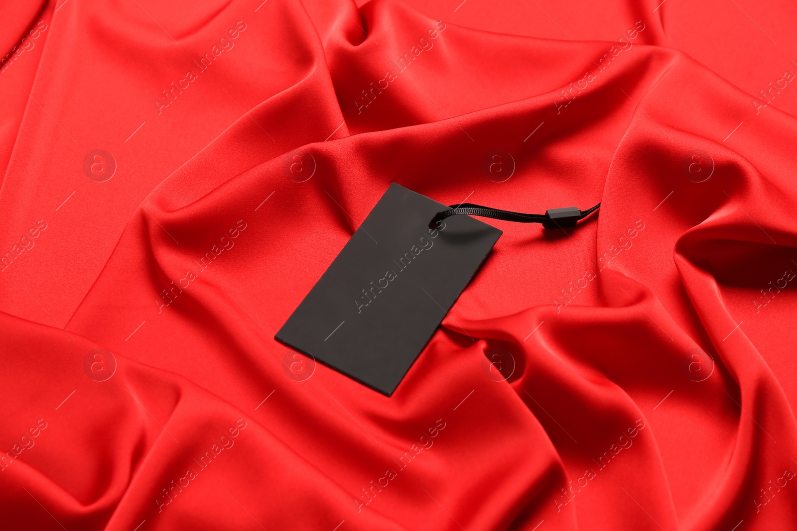 Photo of Blank black tag on red silky fabric. Space for text