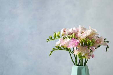 Beautiful blooming freesias in vase against blue background. Space for text