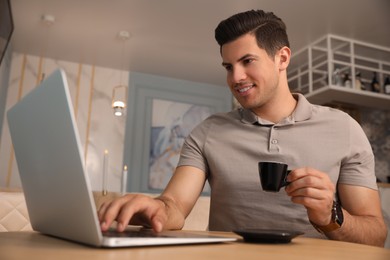 Man with cup of coffee working on laptop at cafe in morning