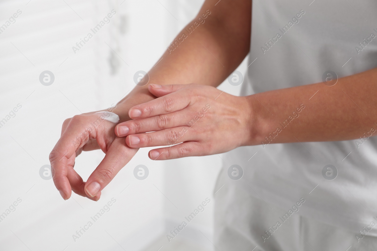 Photo of Woman applying cosmetic cream onto hand on blurred background, closeup