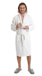 Young man in bathrobe with cup of drink on white background