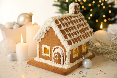 Photo of Beautiful gingerbread house decorated with icing and candles on white table