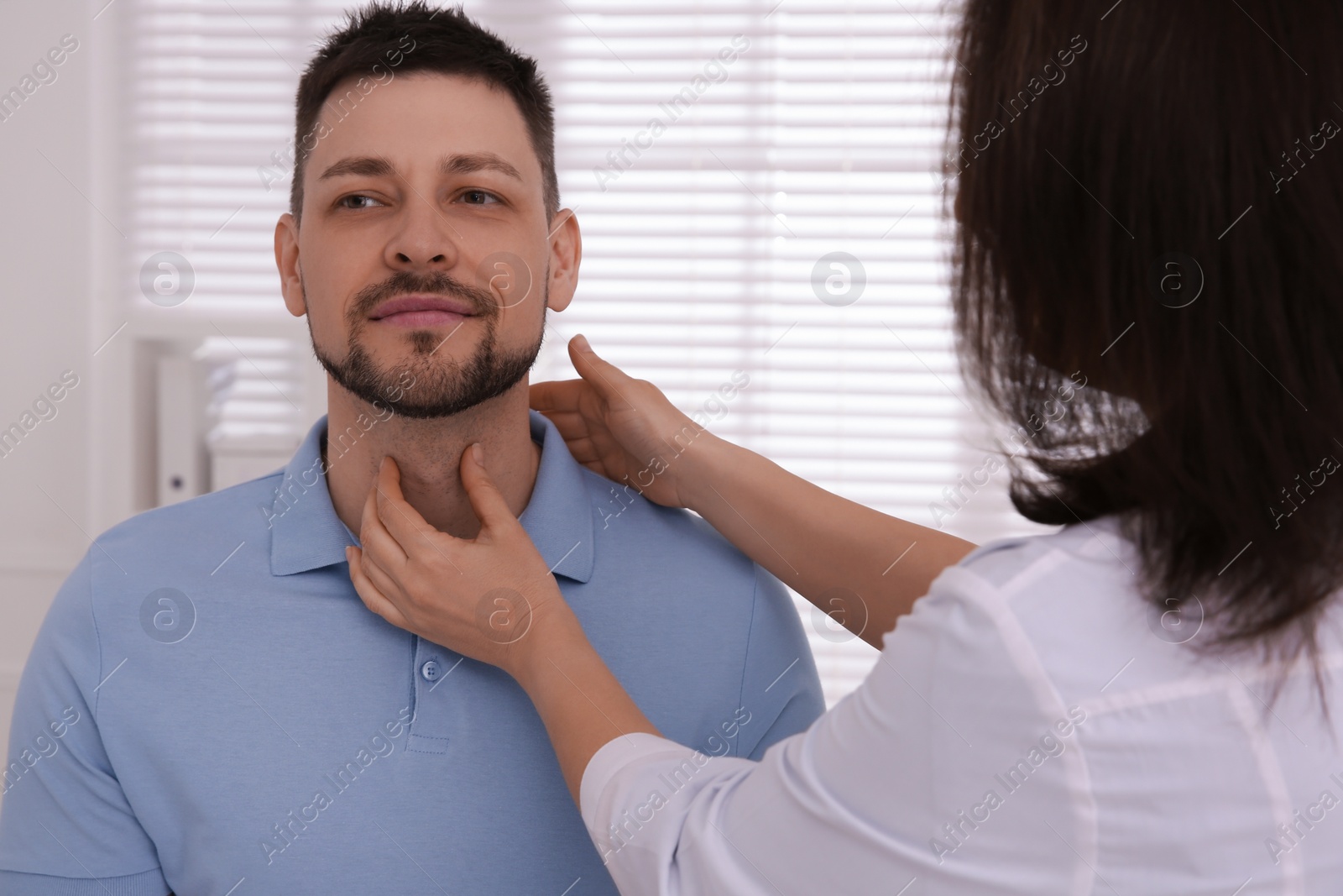 Photo of Doctor examining thyroid gland of patient indoors