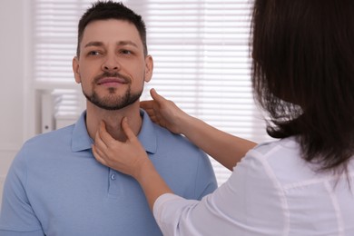 Photo of Doctor examining thyroid gland of patient indoors