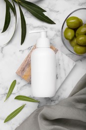 Photo of Bottle of cosmetic product with olive essential oil and leaves on white marble table, flat lay