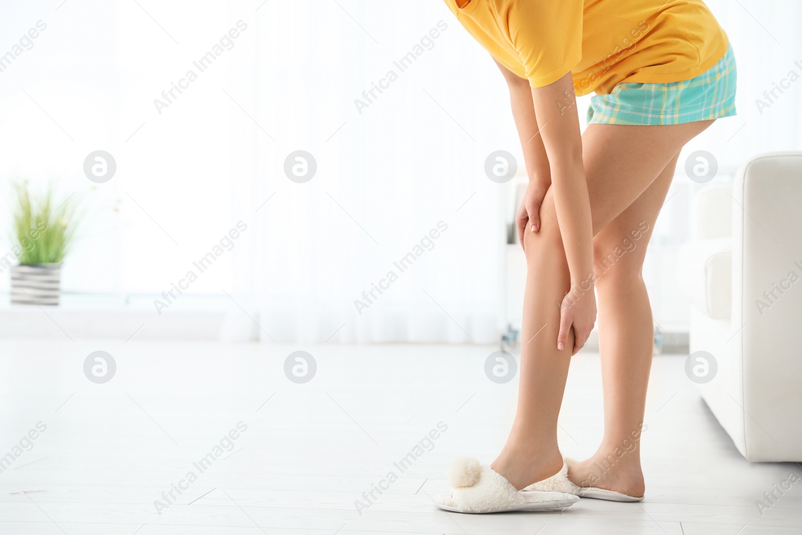 Photo of Young woman suffering from leg pain at home, closeup. Space for text