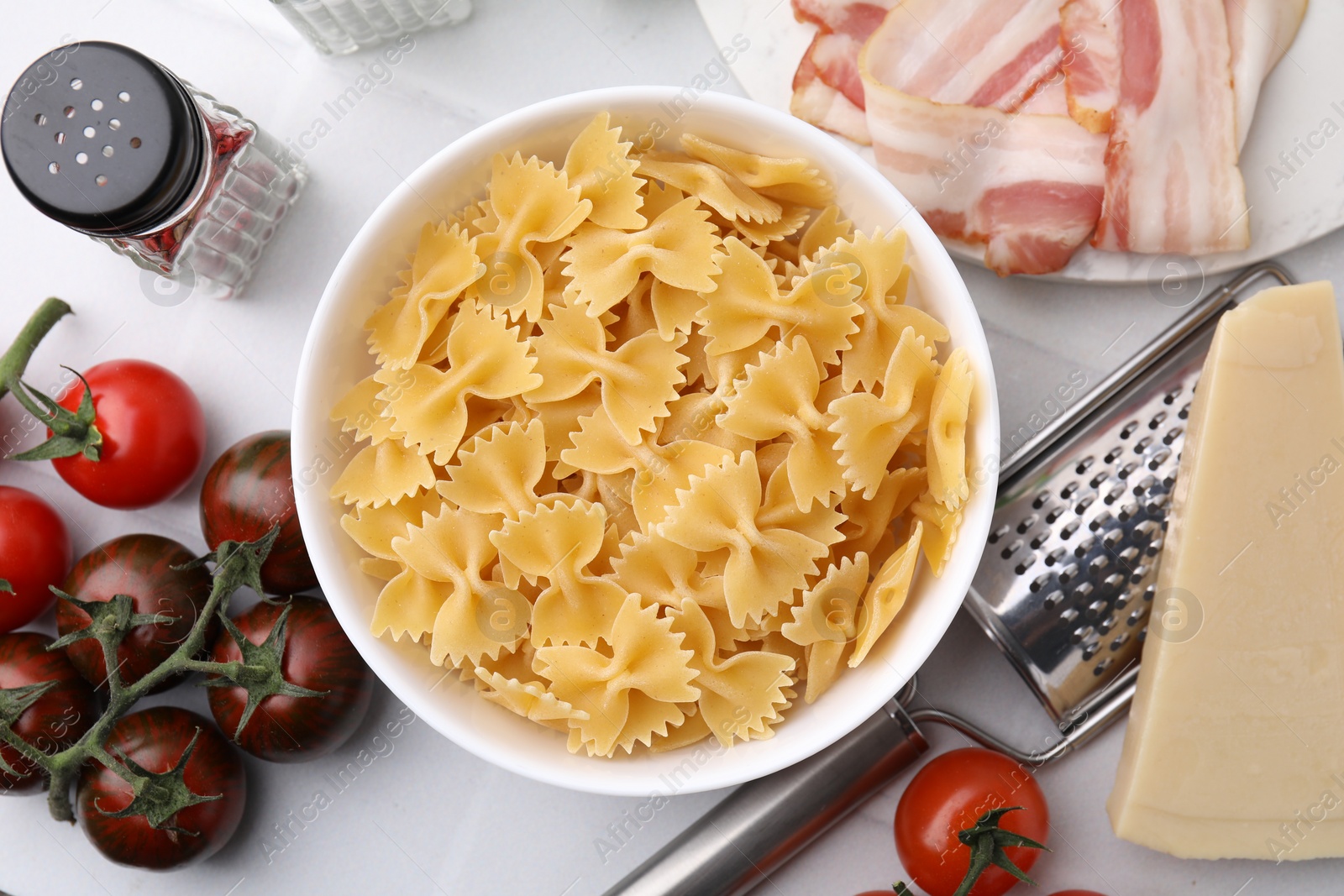 Photo of Raw pasta, bacon and fresh ingredients on white tiled table, flat lay