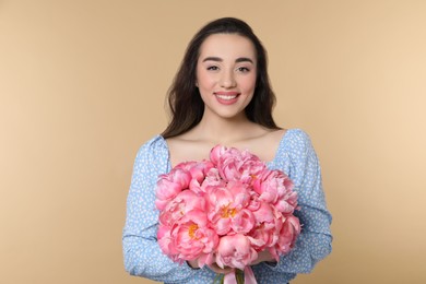 Beautiful young woman with bouquet of pink peonies on beige background