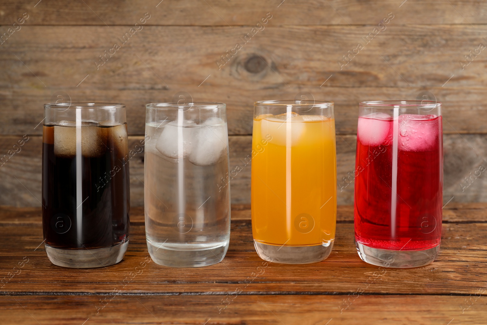 Photo of Glasses of different refreshing soda water with ice cubes on wooden table