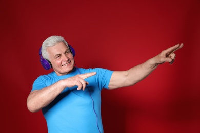 Mature man enjoying music in headphones on color background