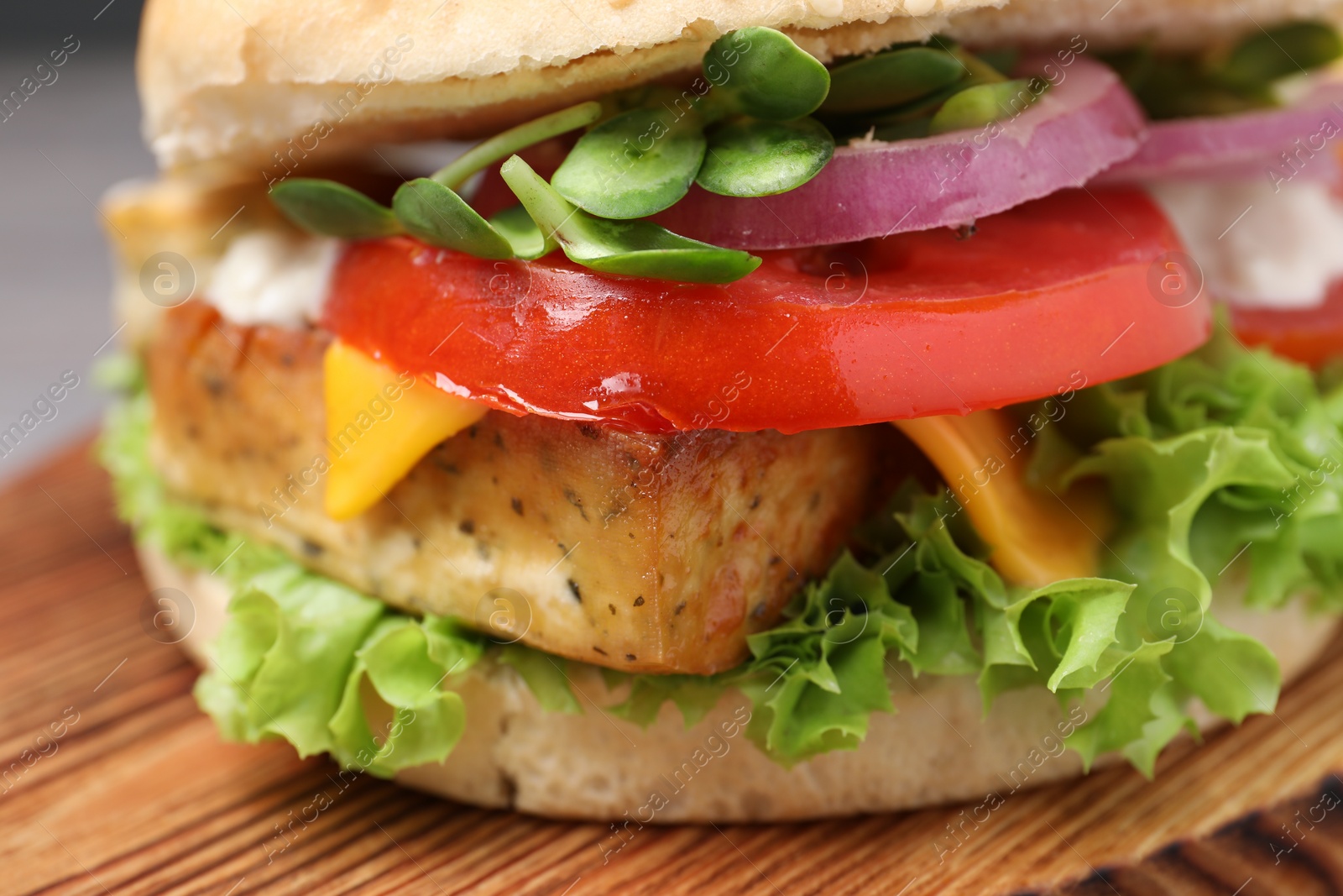 Photo of Delicious burger with tofu and fresh vegetables on wooden board, closeup