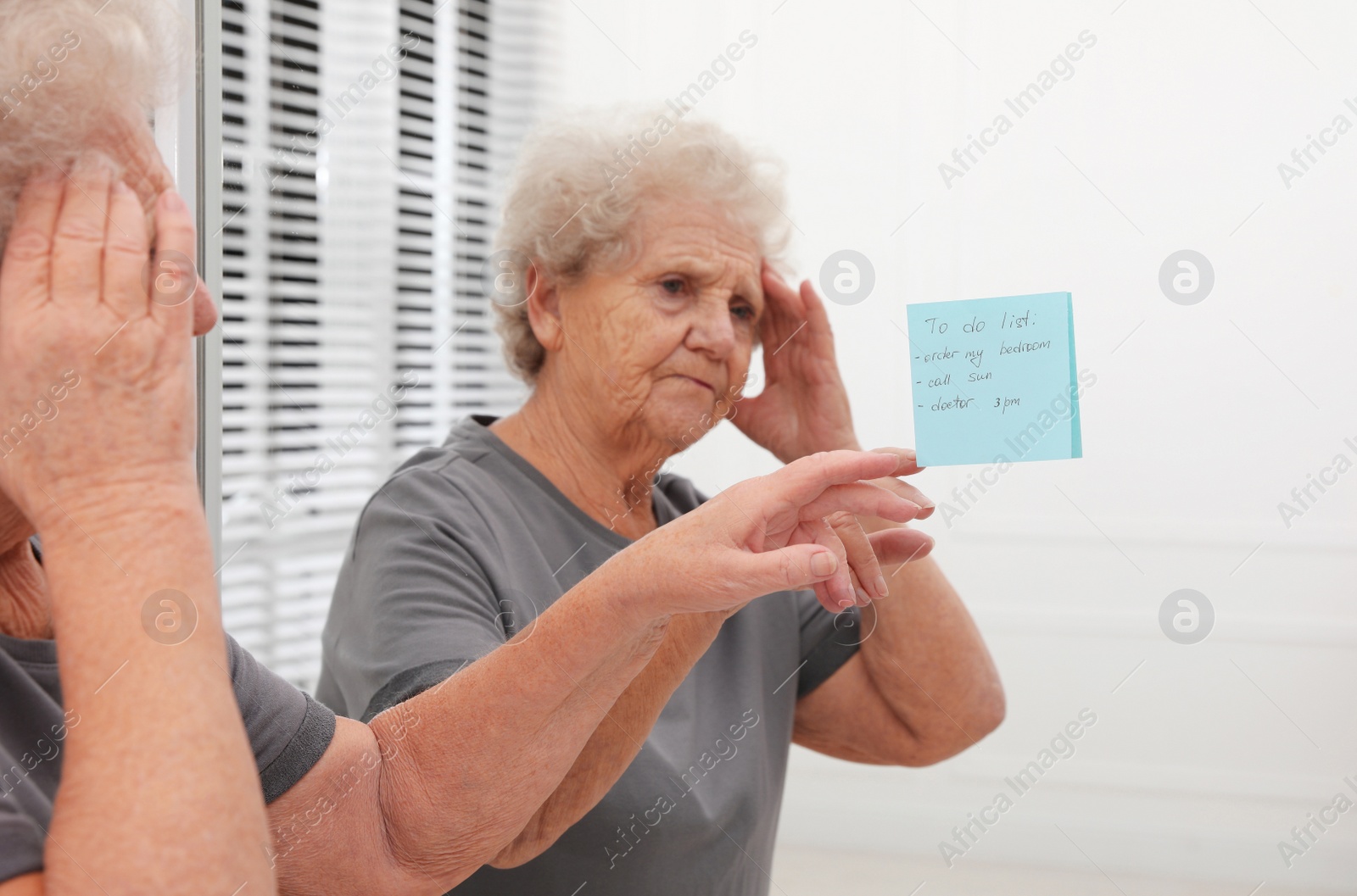 Photo of Senior woman looking at reminder note indoors. Age-related memory impairment