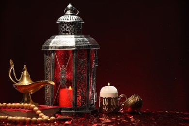 Photo of Arabic lantern, Quran, misbaha, burning candle and Aladdin magic lamp on shiny red table. Space for text