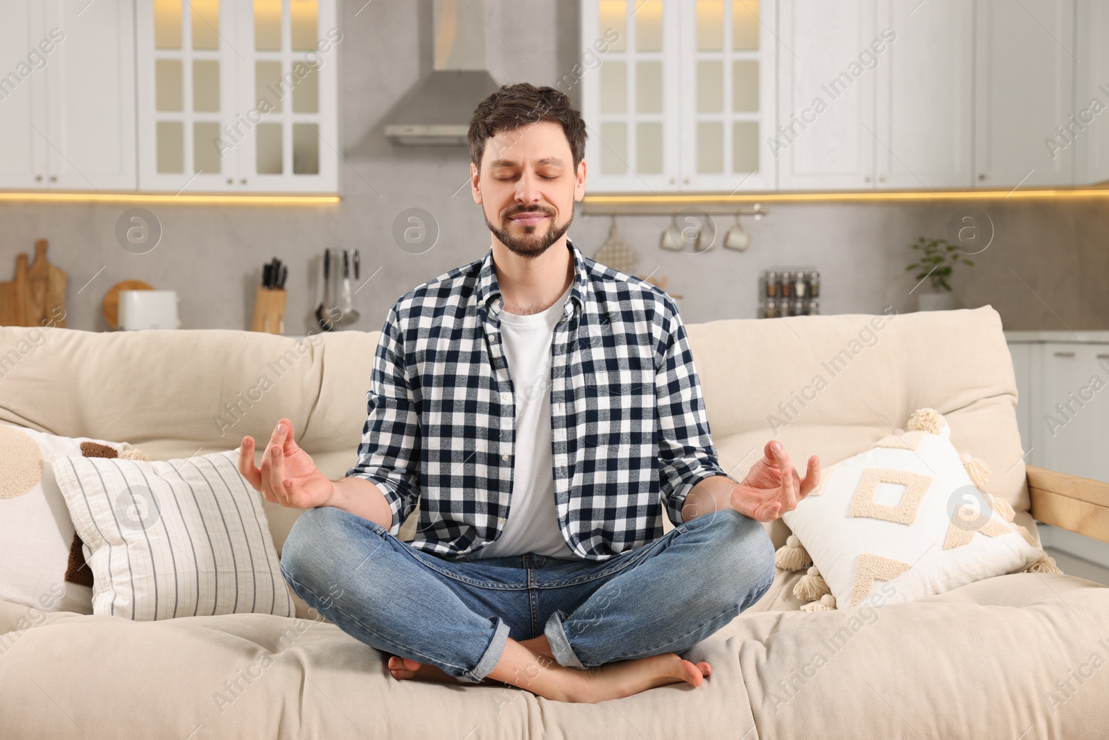 Photo of Man meditating on sofa at home. Harmony and zen