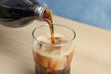 Photo of Pouring refreshing soda drink into glass on wooden table, closeup