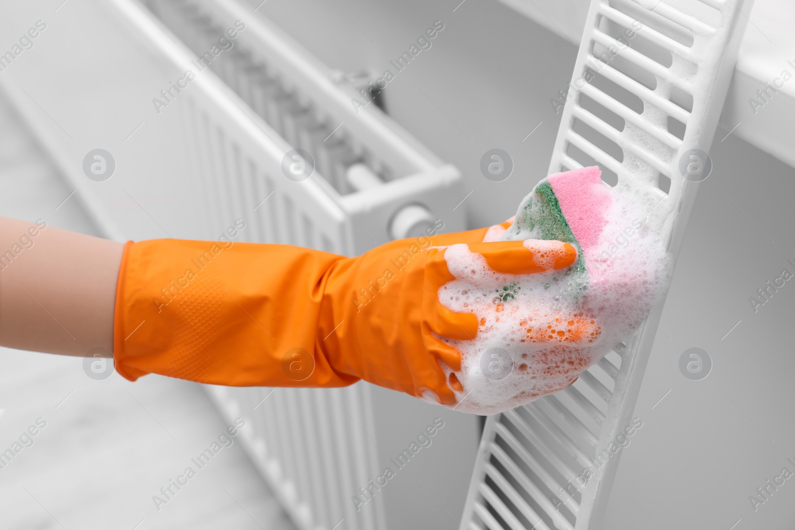 Photo of Woman washing radiator grill with sponge and detergent indoors, closeup