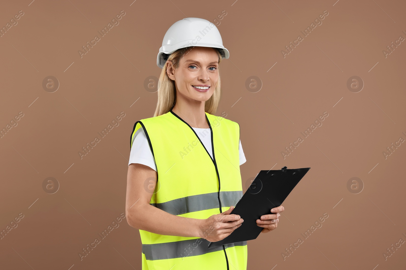 Photo of Engineer in hard hat holding clipboard on brown background