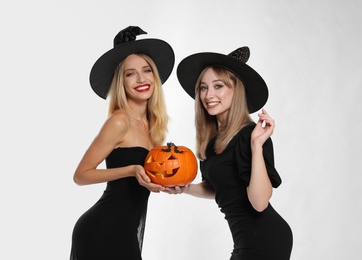 Photo of Beautiful women in witch costumes with jack o'lantern on white background. Halloween party