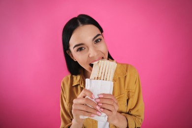 Young woman eating delicious shawarma on pink background