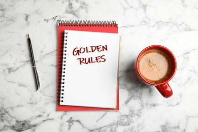 Flat lay composition of notebook with phrase GOLDEN RULES and coffee on white marble background